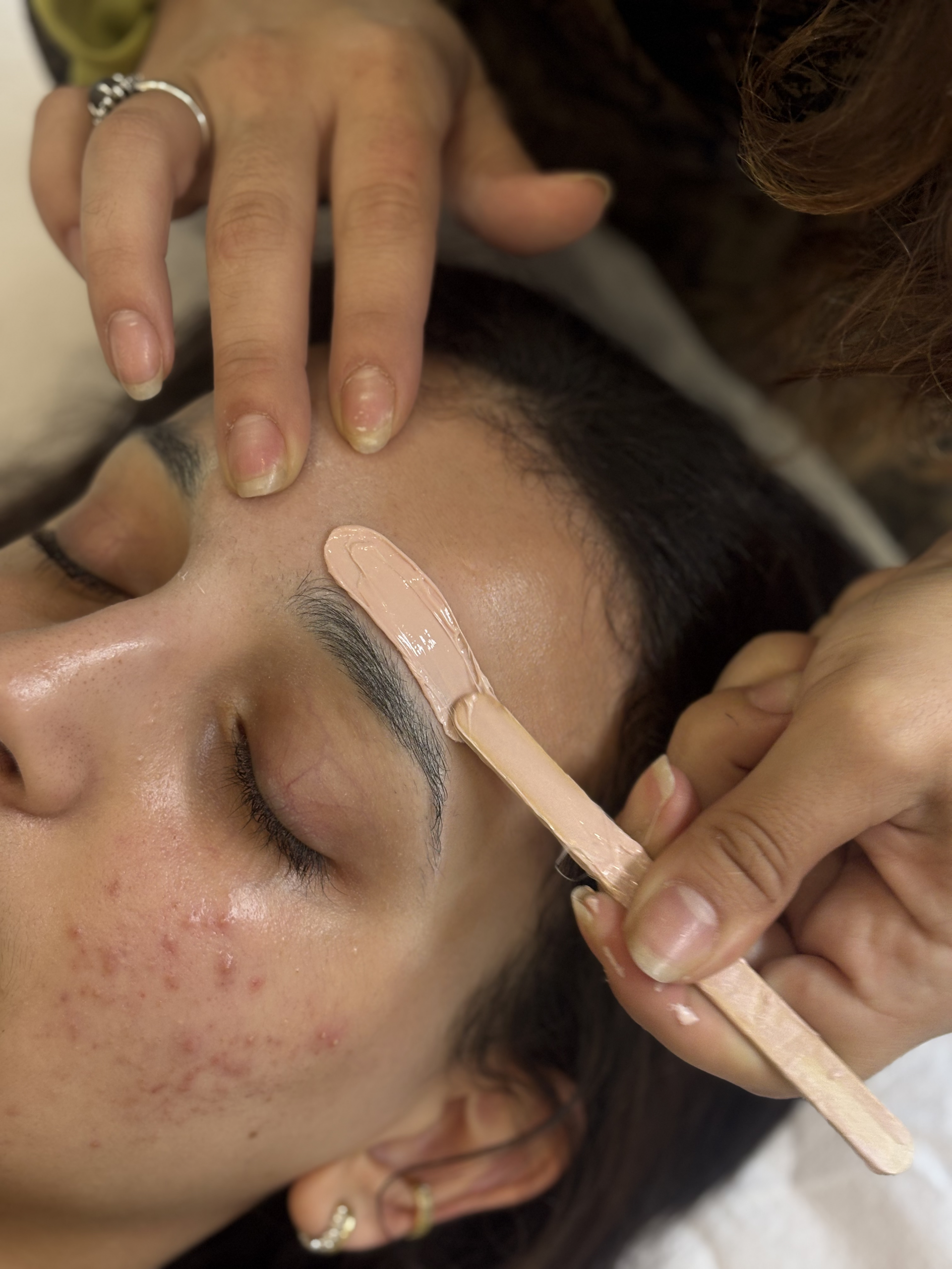 Épilation des sourcils à la cire chaude sur cliente allongée en institut de beauté
