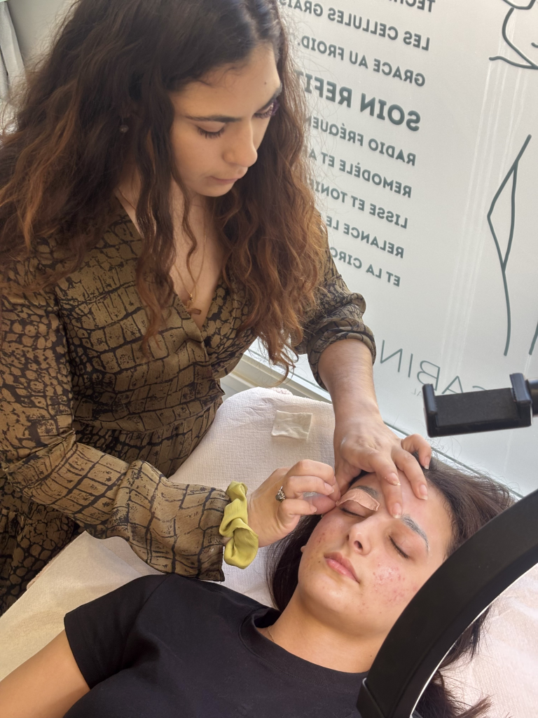Esthéticienne réalisant une épilation des sourcils à la cire sur une cliente en cabine de soins